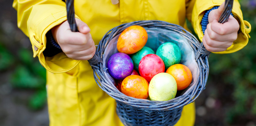 Child in a raincoat holding a basket full of Easter eggs